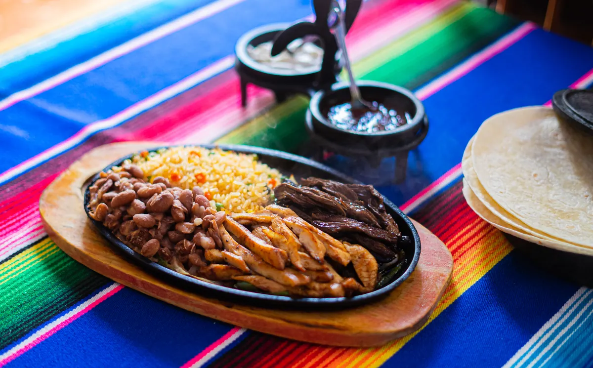 Fajitas en sartén de hierro con tortillas, arroz y frijoles